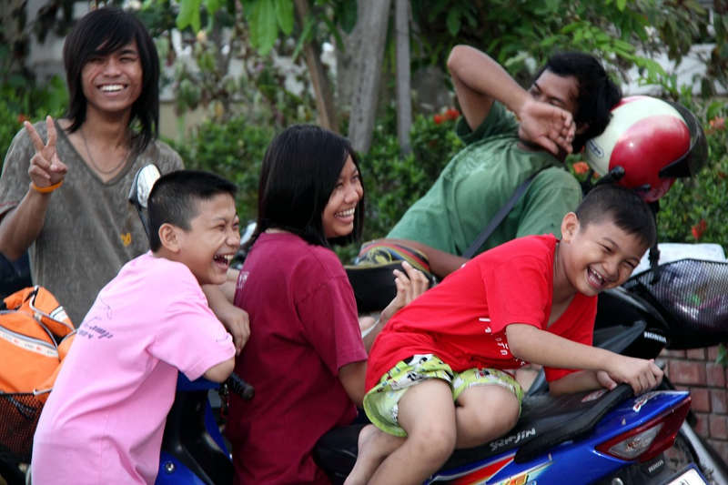 Een Thaise familie op en rondom een scooter die hardop aan het lachen zijn.